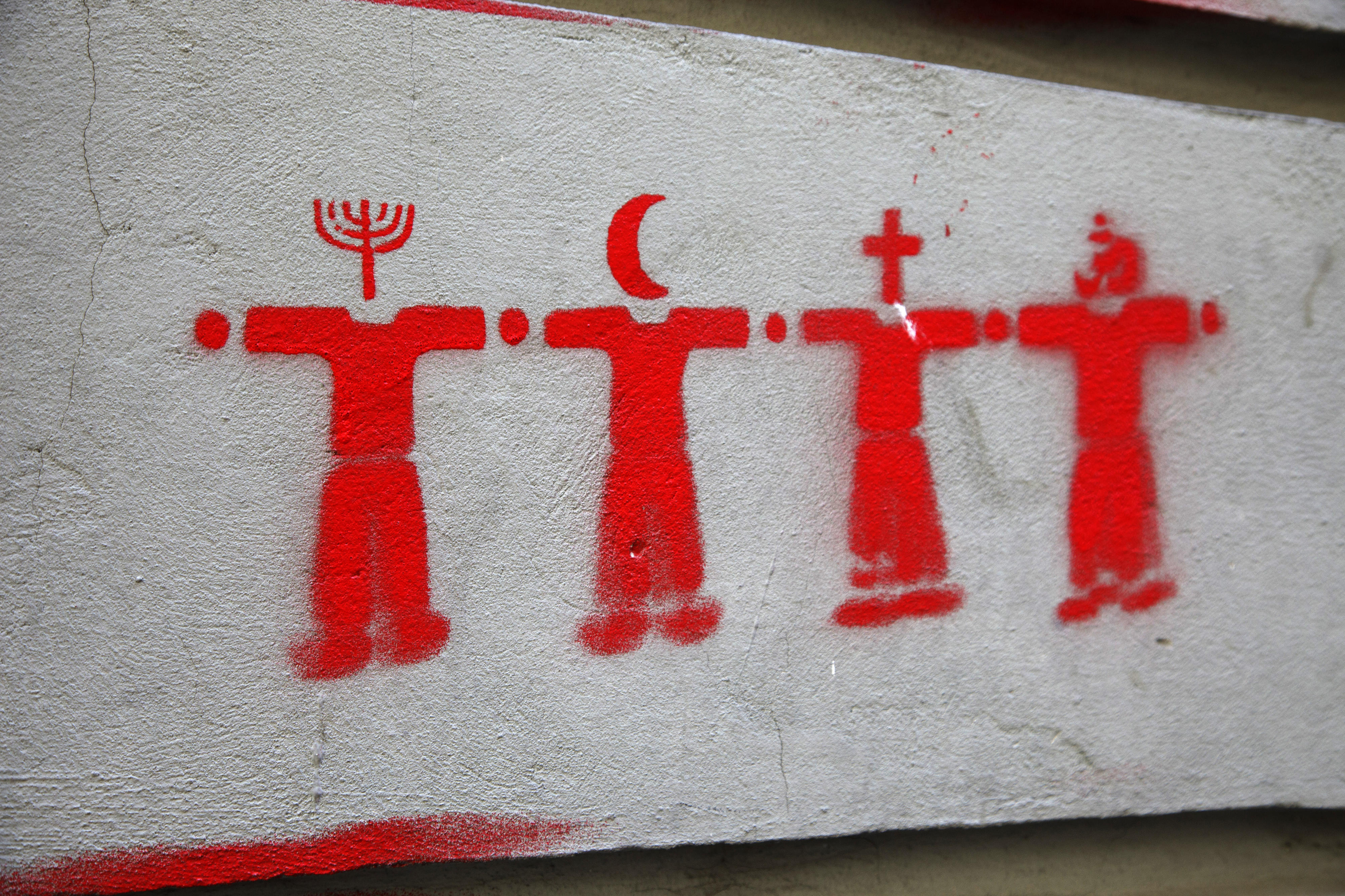 Symbolbild Weltreligionen, dargestellt in Form eines Graffitis auf einer Zementoberfläche: Vier rote Figuren symbolisieren verschiedene Religionen 
